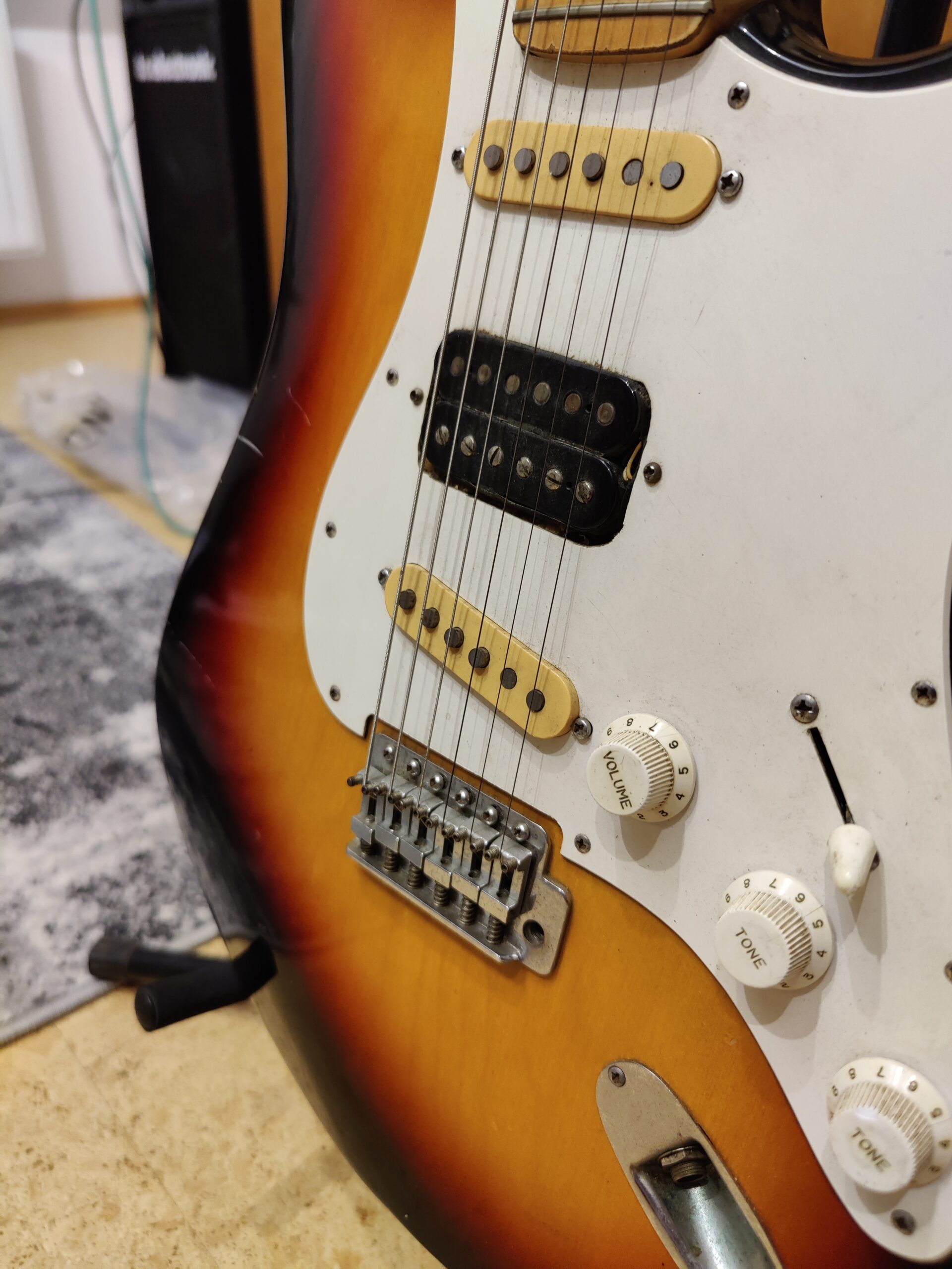 Two cream single-coil pickups and a black middle-position humbucker on a sunburst Isonez Stratocaster-type guitar.