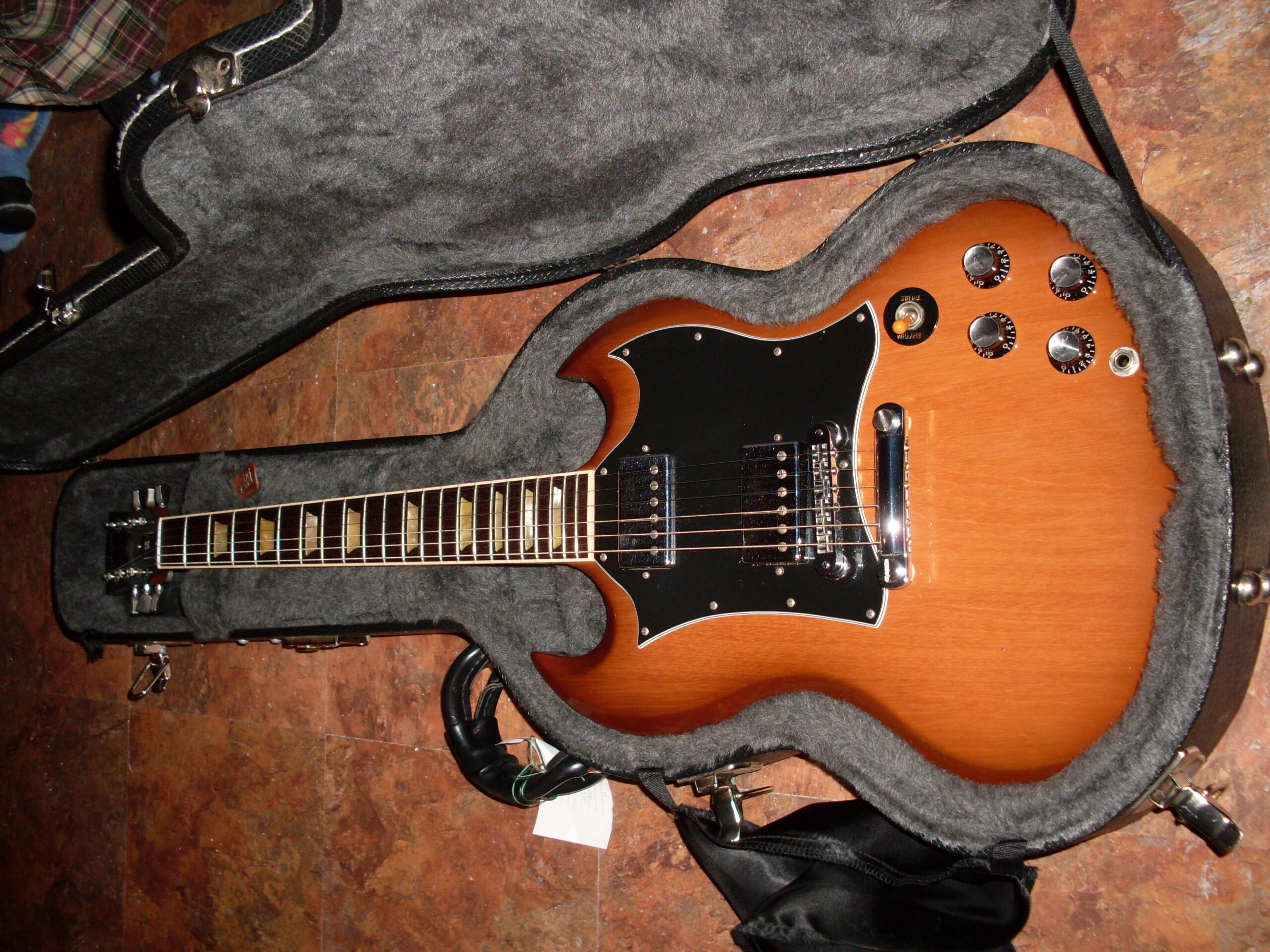 Brown Gibson SG Standard with black pickguard shown from headstock to body in an open guitar case.