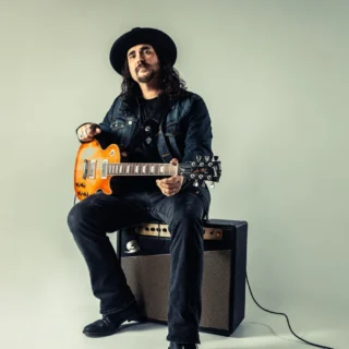 Alastair Greene holding an electric guitar in an archival publicity photograph.