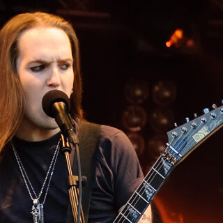 Alexi Laiho singing into a microphone at Ilosaarirock in 2009, with his guitar neck visible.