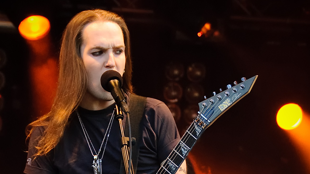Alexi Laiho singing into a microphone at Ilosaarirock in 2009, with his guitar neck visible.