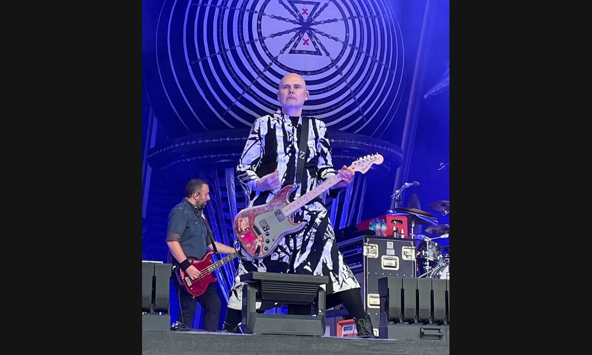 Billy Corgan on stage in 2025 with his head, hands and entire worn red electric guitar visible in the full concert photograph.