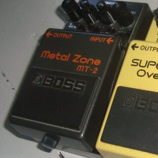 A black Boss MT-2 Metal Zone pedal with its full enclosure and controls visible, with an adjacent yellow pedal edge.