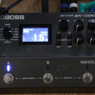 Complete Boss RV-500 reverb pedal with its illuminated display, six control knobs and three footswitches, with connected cables visible at the top.