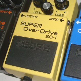 A yellow Boss SD-1 pedal with its full enclosure and three knobs visible, with edges of neighboring pedals.