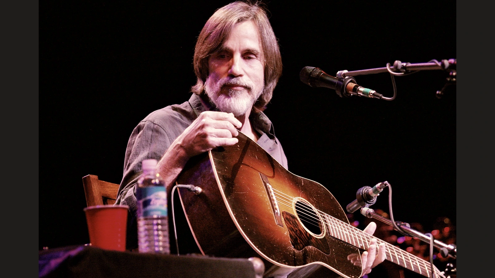 Jackson Browne holding an acoustic guitar on stage in 2008