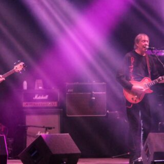 Camel performing under purple stage lights at Ramblin’ Man Fair in 2015, with guitar, bass and keyboards visible.