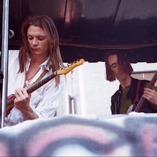Chris Whitley, left, playing guitar alongside bassist Alan Gevaert at an outdoor benefit performance in New York City in the 1990s.