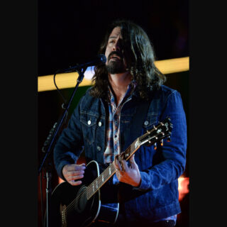 Dave Grohl singing and playing an acoustic guitar at the Concert for Valor in Washington, D.C., in 2014; the complete source photograph appears on a plain dark canvas.