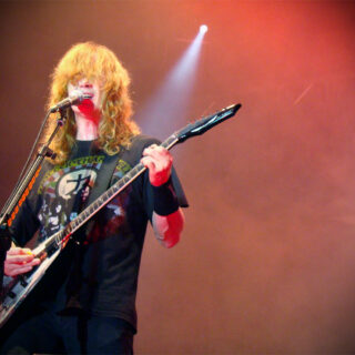 Dave Mustaine singing into a microphone while playing a V-shaped electric guitar in Venezuela.