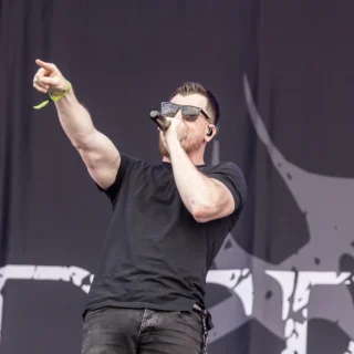 Defects vocalist performing at Rockharz in 2025, holding a microphone and pointing toward the audience.