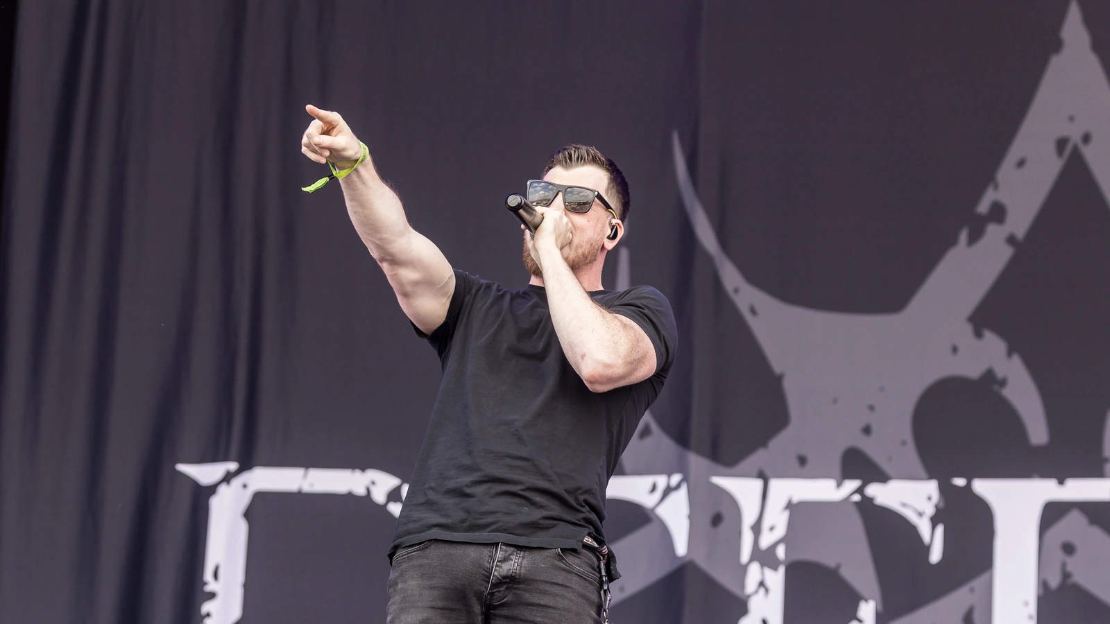 Defects vocalist performing at Rockharz in 2025, holding a microphone and pointing toward the audience.