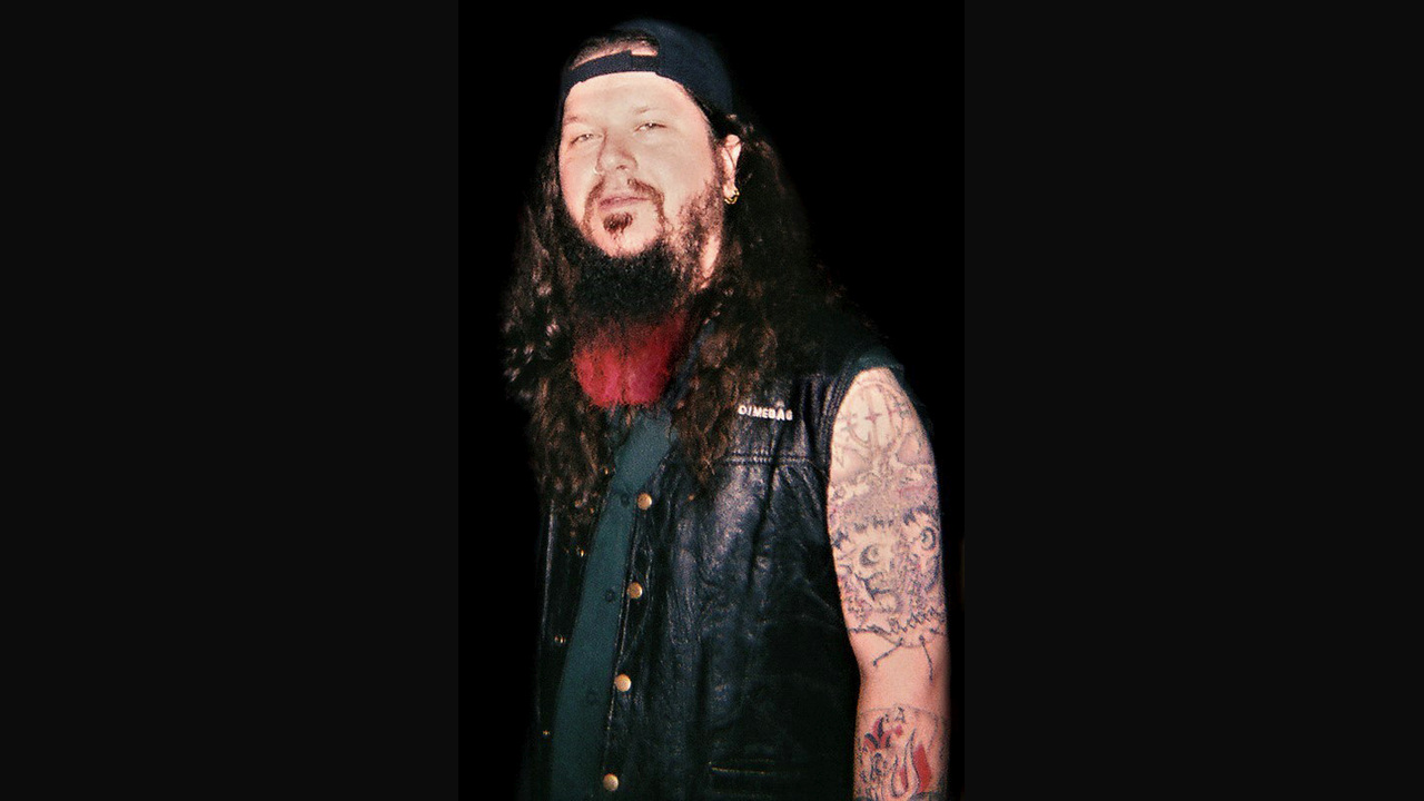 Dimebag Darrell wearing a backwards black cap and sleeveless vest, with long hair and a red-tipped beard.