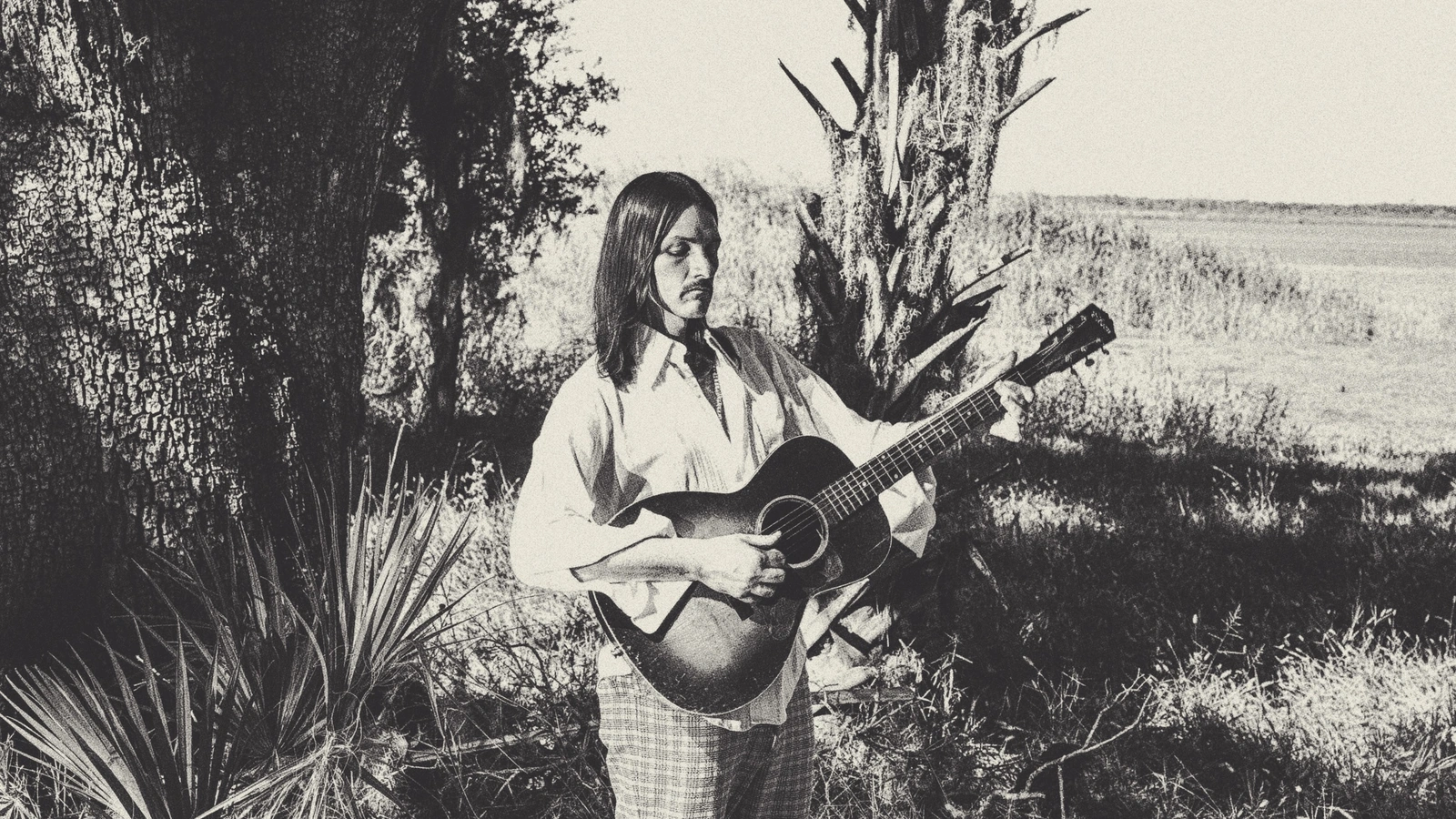 Duane Betts playing an acoustic guitar outdoors in a black-and-white promotional photograph.