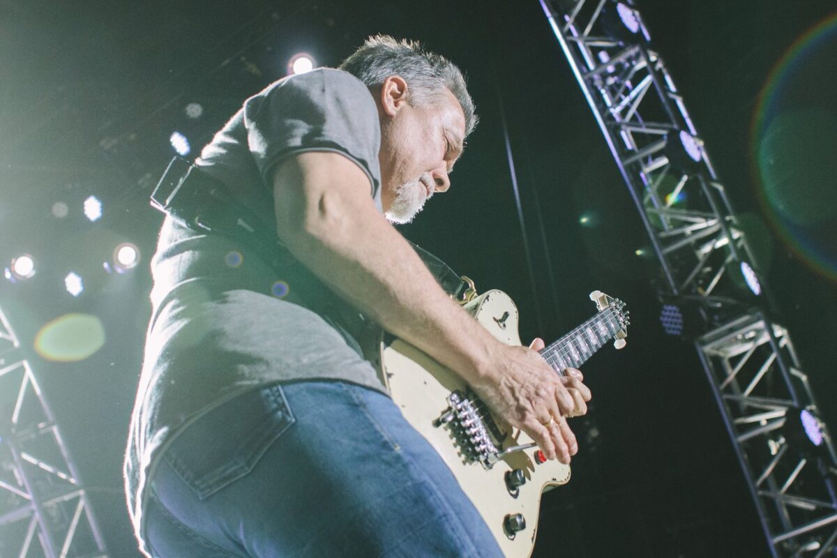 Eddie Van Halen tapping a light-colored electric guitar during a live performance.
