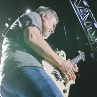 Eddie Van Halen tapping a light-colored electric guitar during a live performance.