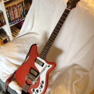 Worn-cherry 2011 Epiphone '66 Wilshire with tremolo, complete instrument resting on a chair.