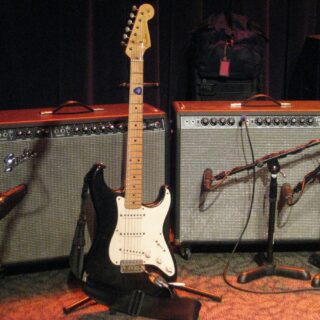 Two Fender Twin Reverb combo amplifiers behind a Stratocaster and stage microphones.