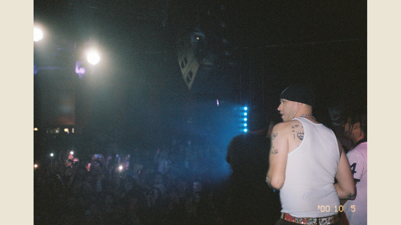 Archival photograph of fish narc in left-facing profile onstage, wearing a black head covering and white sleeveless shirt.