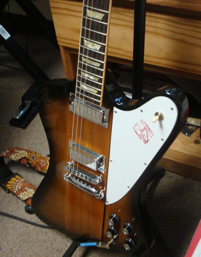 Sunburst Gibson Firebird V body with two covered Firebird pickups, white bird-logo pickguard, bridge, stopbar and four controls.