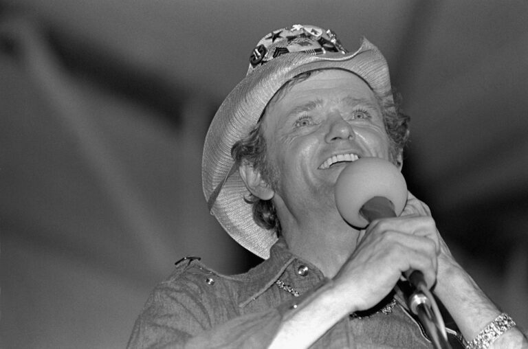 Jerry Reed in a cowboy hat singing into a microphone on stage