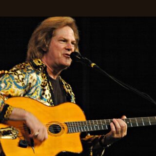 John Jorgenson singing and playing a Selmer-style acoustic guitar.