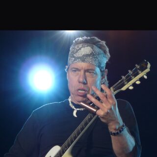 George Thorogood playing a white semi-hollow guitar on stage