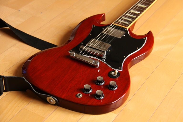 Cherry red Gibson SG Standard electric guitar with black pickguard and two humbuckers lying on a wooden floor