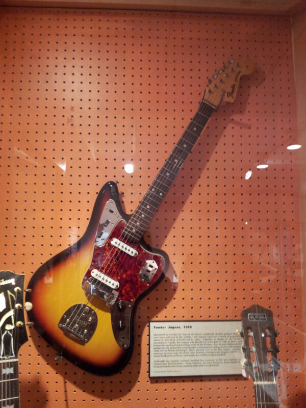 1965 Fender Jaguar in sunburst with tortoiseshell pickguard, hanging on a pegboard in a museum display case
