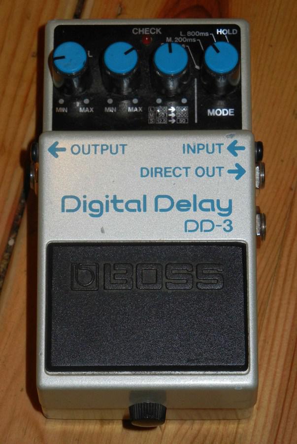 Top-down view of a Boss DD-3 Digital Delay pedal with blue knobs and the Output, Input and Direct Out labels on a wooden floor.