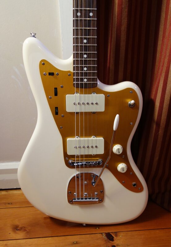 Body of a vintage-white Squier J Mascis Jazzmaster with gold anodised pickguard, two cream single-coil pickups, Adjusto-Matic bridge with tremolo plate and arm, and rosewood fingerboard.