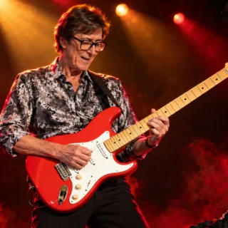 AI-generated editorial illustration of mature Hank Marvin playing a red Strat-style guitar, with amber stage lighting and red-and-black paper textures.
