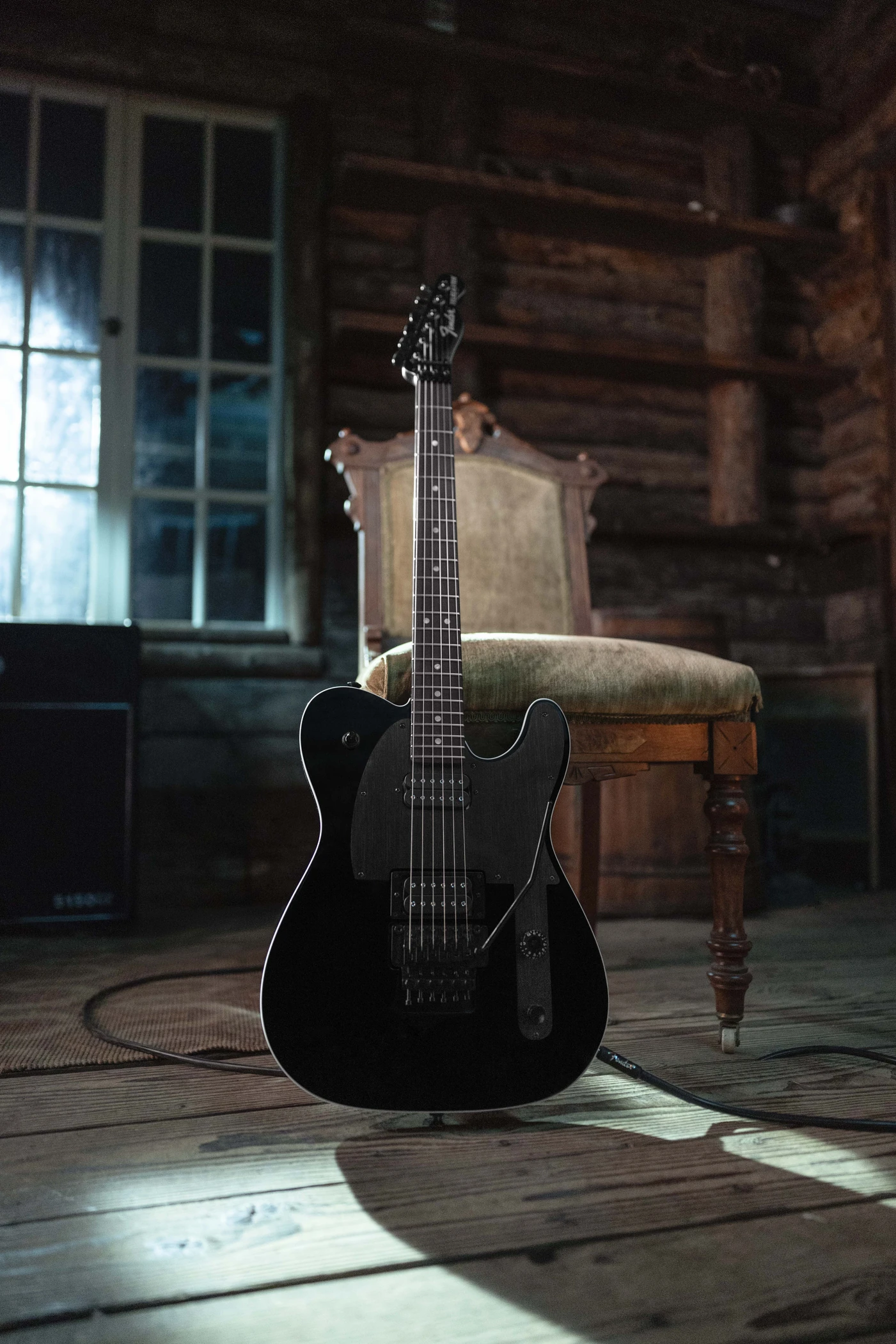 Full black Fender Custom Shop John 5 Phantom Telecaster standing in front of an upholstered chair, with its headstock, neck and body visible.