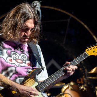 John Frusciante looking down at the fretboard of a worn sunburst electric guitar during a London performance in 2023.