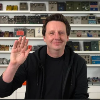 Josh Scott in front of shelves of guitar effects pedals.