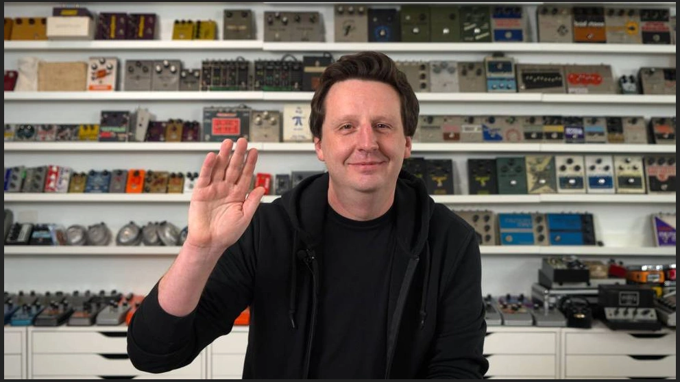 Josh Scott in front of shelves of guitar effects pedals.