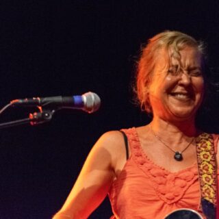 Kristin Hersh laughing on stage with her guitar beside a microphone during an Electric Trio concert in Somerville in 2019.