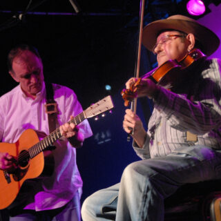 Martin Carthy and Dave Swarbrick at the 2007 BBC Radio 2 Folk Awards, in the complete stage photograph showing an acoustic guitar and fiddle, with dark side margins.