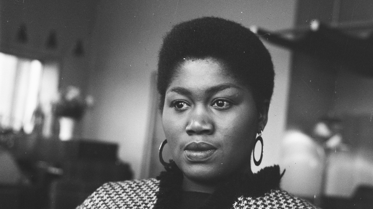 Black-and-white portrait of Odetta wearing hoop earrings and a patterned jacket, with her complete head and shoulders visible.