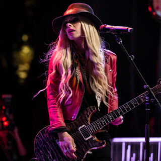 Orianthi playing an electric guitar beside a microphone on stage.