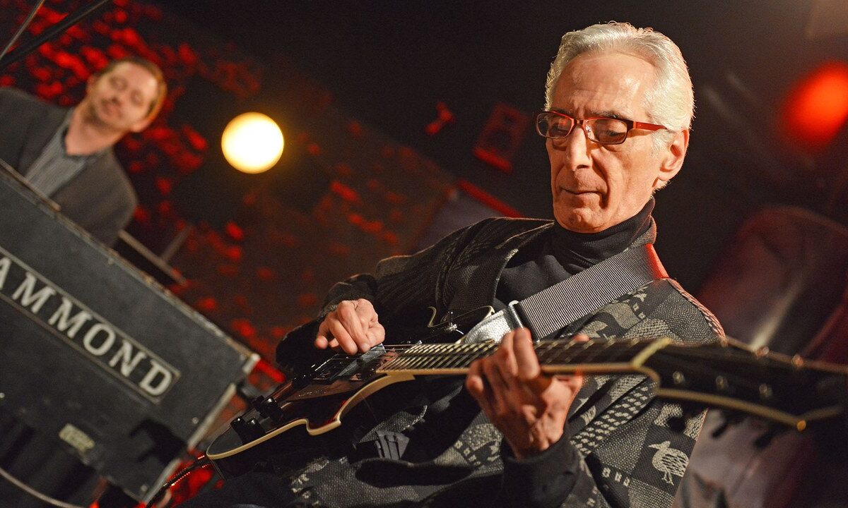 Pat Martino playing guitar onstage at Bielska Zadymka Jazzowa, with his full head and both hands visible and an organist in the background.