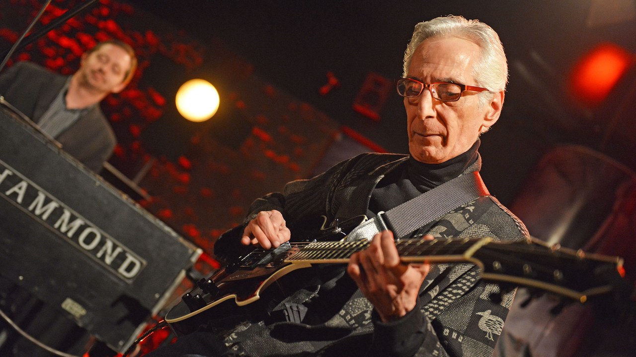 Pat Martino playing guitar onstage at Bielska Zadymka Jazzowa, with his full head and both hands visible and an organist in the background.