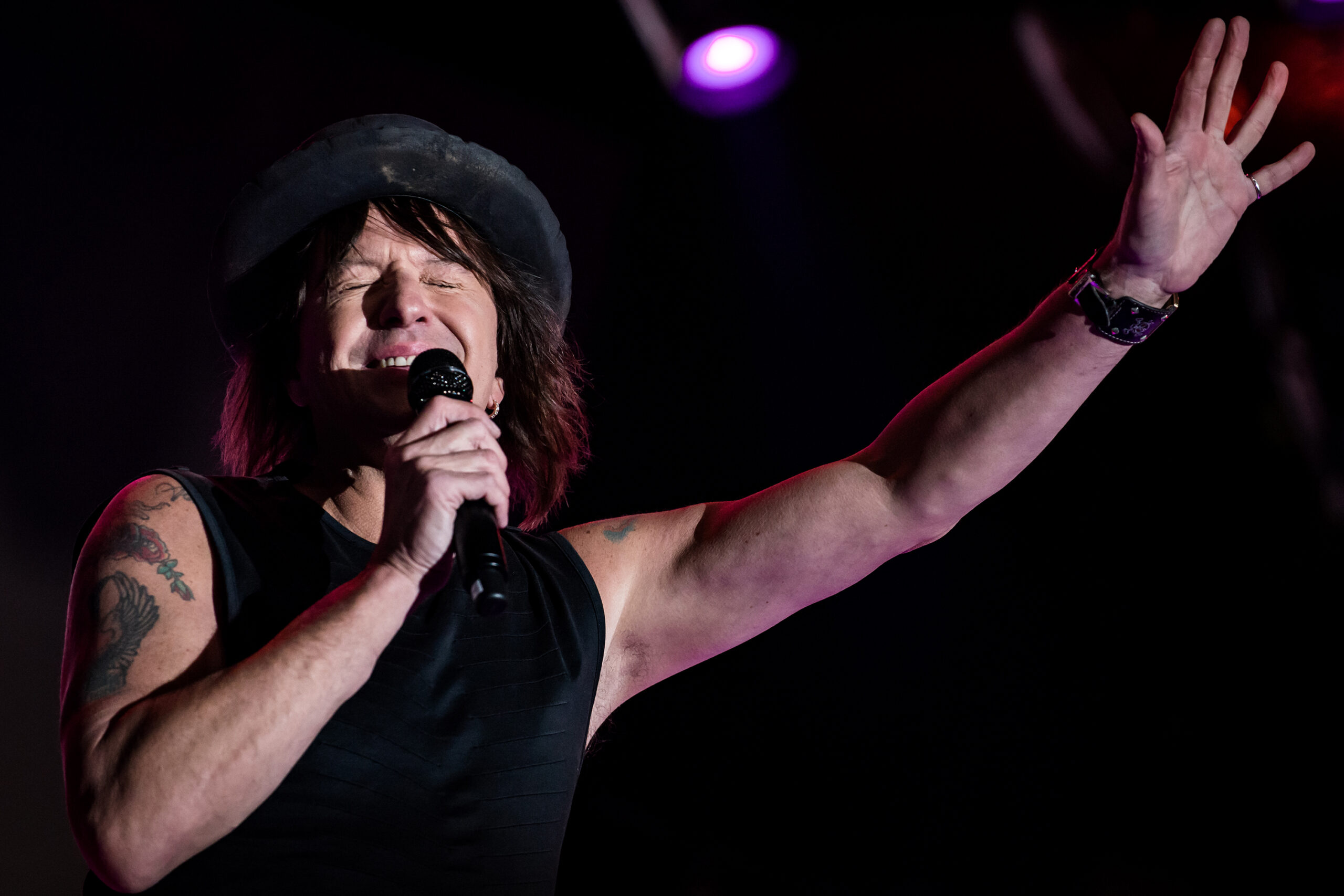 Richie Sambora singing into a microphone with one arm raised at the Winter NAMM Show in 2017.