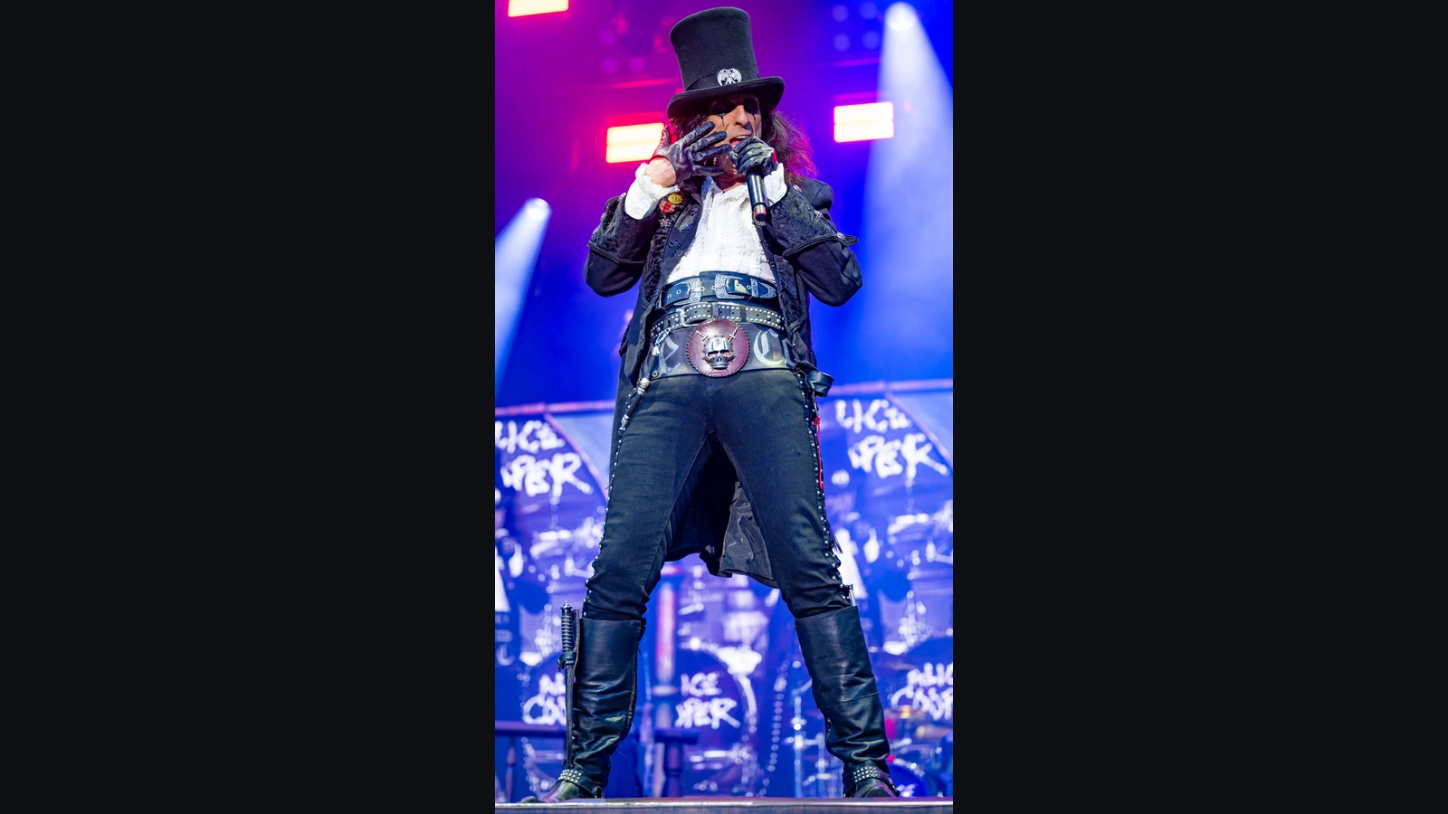 Alice Cooper sings into a microphone wearing a top hat on stage in Nuremberg in 2024.