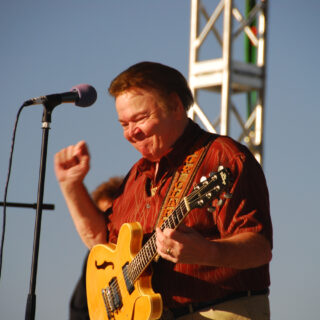 Roy Clark performing with an electric guitar at the Huck Finn Festival in 2007; the complete source photograph on a dark canvas.