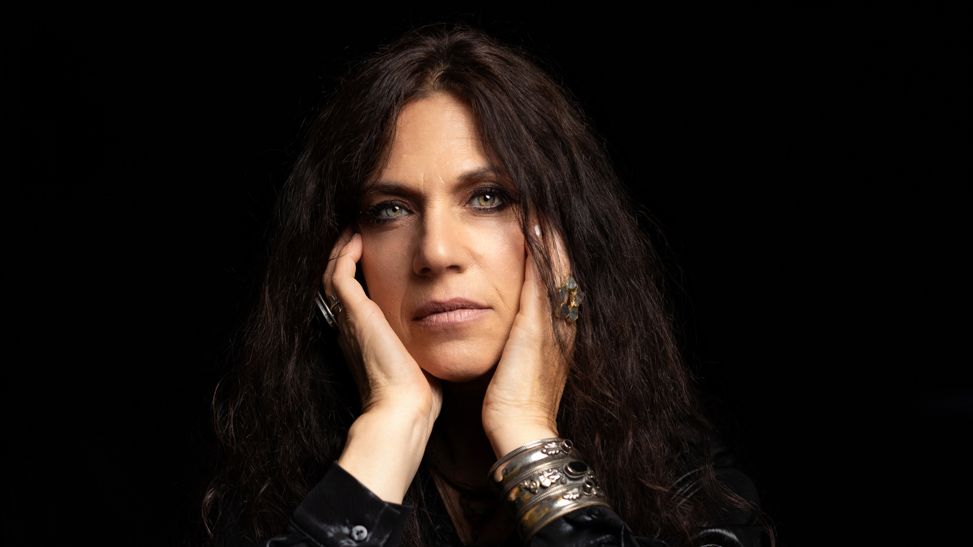 Sari Schorr in a black leather jacket, with her hands beside her face.