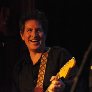 Steve Wynn smiling onstage with a guitar during a Baseball Project performance.