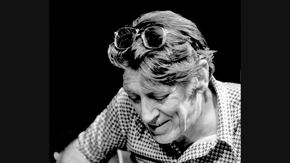 Tal Farlow looking down while performing, in a black-and-white portrait with glasses resting on his head.