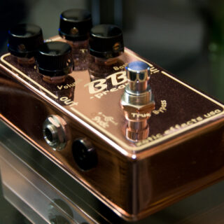 An earlier copper-finish Xotic BB Preamp pedal with four black knobs and one footswitch, photographed at an angle with its reflection.
