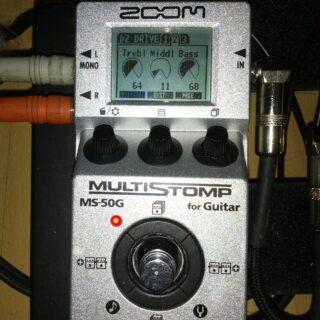 A complete silver Zoom MS-50G MultiStomp for Guitar pedal with three control knobs, screen and one footswitch, connected on a pedalboard.